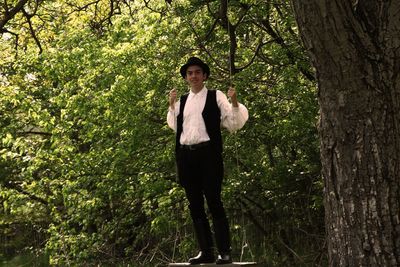 Portrait of teenage boy standing on swing against plants