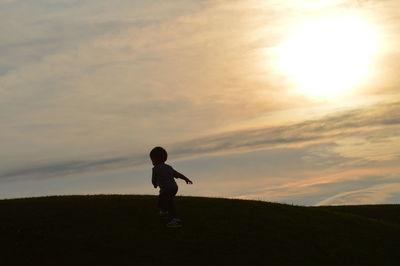 Silhouette boy standing against sky during sunset