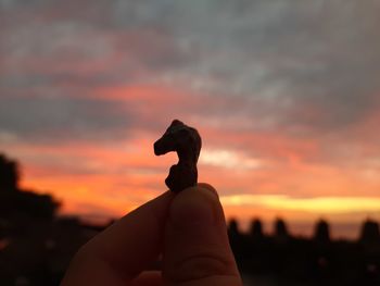 Cropped hand holding stone against sky during sunset