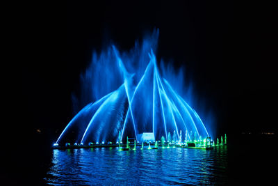 Illuminated fountains against sky at night