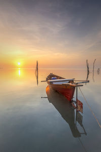 Fishing boat moored in sea against sky during sunset