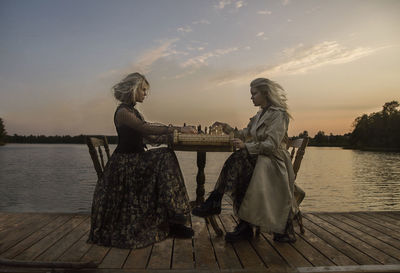 Side view of women sitting on pier against sky during sunset