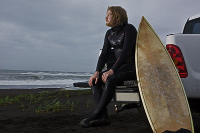 Surfer sits on back of his pick up truck and watches the ocean