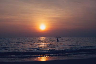 Silhouette person on sea against sky during sunset