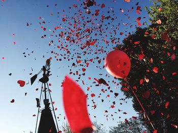 Low angle view of red confetti and balloon against sky