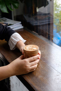 Copped hands of woman holding coffee cup on table in cafe