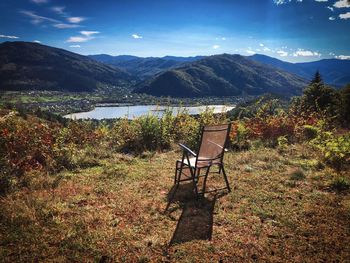 Empty chair in front of mountains and lake on a day with blue sky