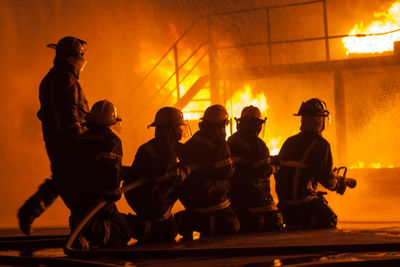 Silhouette firefighters spraying water on fire at night