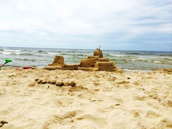 Sand castle at beach against cloudy sky