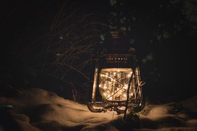 Close-up of illuminated string lights in lantern on sand at night