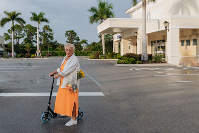 Portrait of  eldery women in orang dress on scooter with palm tree on the background