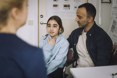 Girl explaining illness to nurse while sitting next to father in clinic