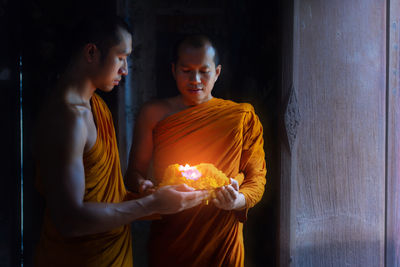 Monks wearing traditional clothing holding illuminated light in temple