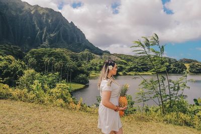 Side view of young woman holding pineapple while standing on land