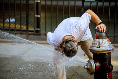 Man washing face in flowing water from fire hydrant in city