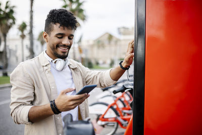 Smiling man using mobile phone at bicycle parking station