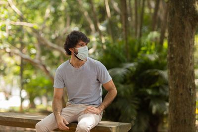 Handsome man wearing a medical protective mask on his face on a sunny day at park.