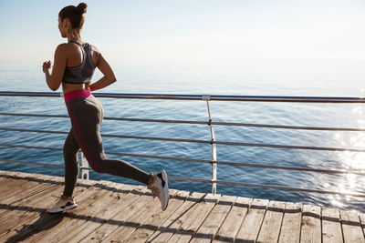 Full length of woman running by railing against sea