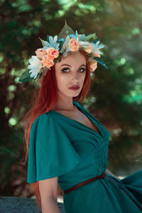 Portrait of beautiful woman wearing flowers while standing against trees