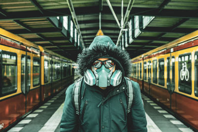 Portrait of man wearing mask standing at railroad station platform