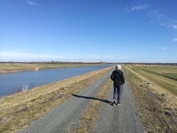 Rear view of man walking on road against sky