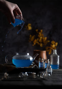 Butterfly pea flower tea blue tea in glass teapot with hand pouring tea with drips moody tones