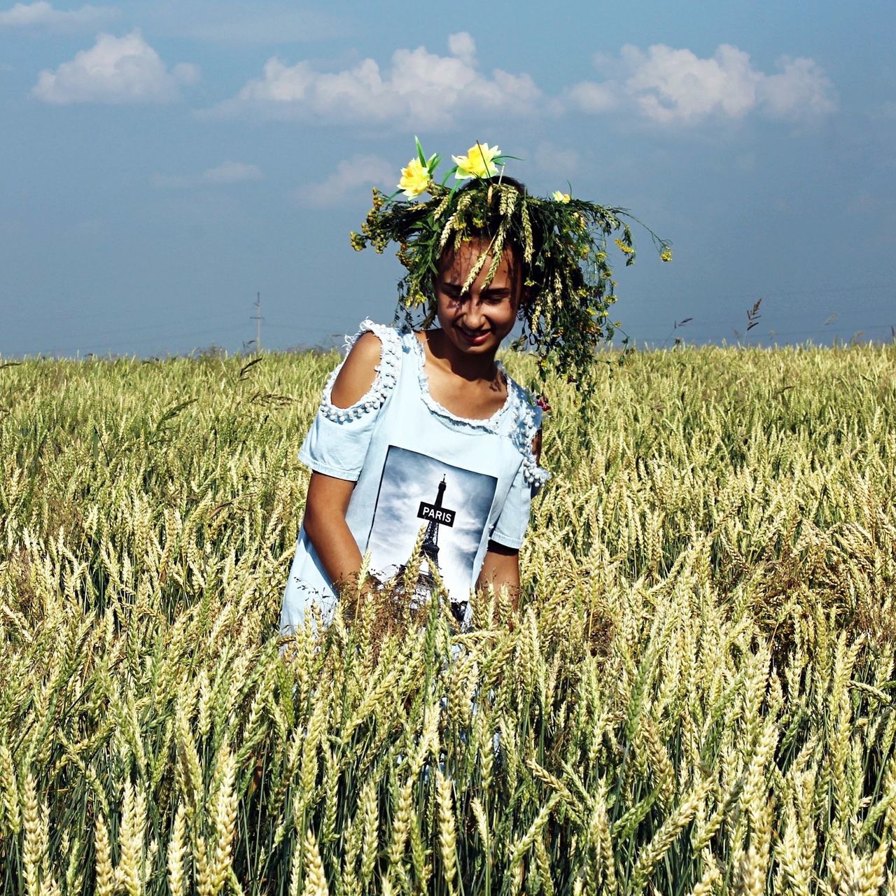 grass, sky, front view, young adult, field, smiling, leisure activity, casual clothing, lifestyles, person, sunlight, young women, growth, standing, plant, nature, day, summer, outdoors, green color, curly hair, cloud - sky, cloud, tranquility, looking at camera, scenics, grassy, beauty in nature