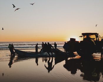 Silhouette people on beach against sky during sunset