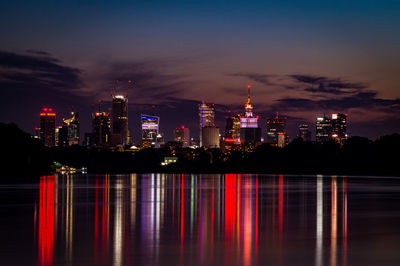 Illuminated buildings by sea against sky at night