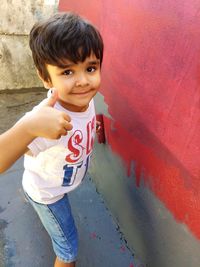 Portrait of boy gesturing thumbs up while standing against wall