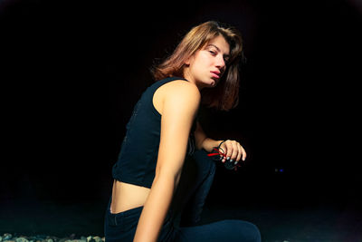 Portrait of woman sitting against black background