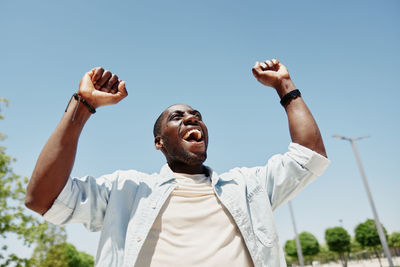 Low angle view of man with arms raised against sky