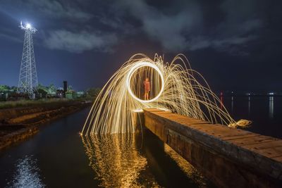 Illuminated ferris wheel by river against sky at night