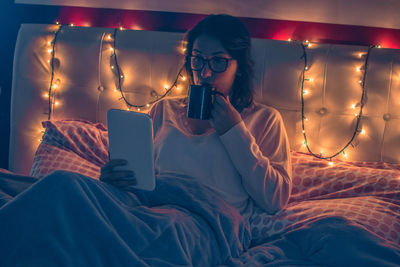 Young woman using digital tablet while sitting on bed at home