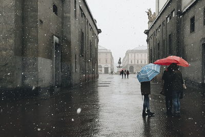 Women with umbrella standing on street during snowfall