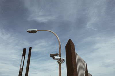 Security cameras on street light against cloudy sky