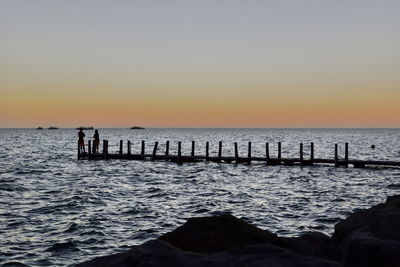 Silhouette wooden posts in sea against clear sky
