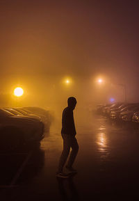 Silhouette man standing on illuminated street against sky at night