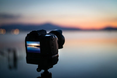 Close-up of camera against sea and sky during sunset