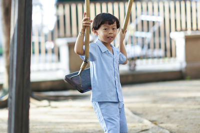 Cute boy holding swing while standing outdoors in playground 