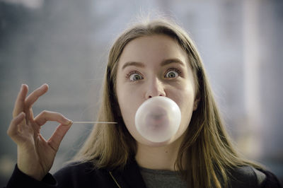 Close-up portrait of beautiful young woman blowing bubble gum and holding toothpick