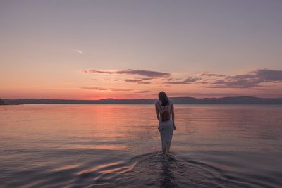 Rear view of woman standing at beach during sunset