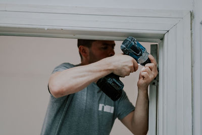 A young man is drilling with a drill in a doorway.