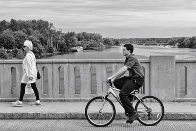 Side view of man riding bicycle on railing against sky
