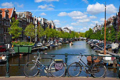 Bicycles on river by buildings in city against sky