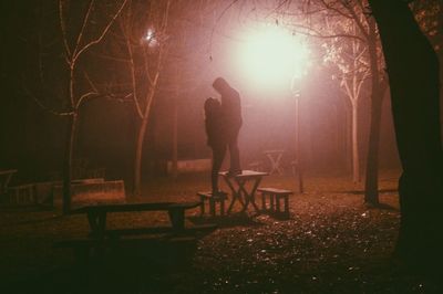 Couple standing on picnic table at park during night