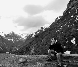 Young woman sitting on mountain against sky