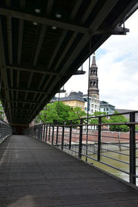 Footbridge over footpath in city against sky