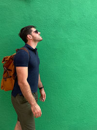 Young man looking away while standing against green wall