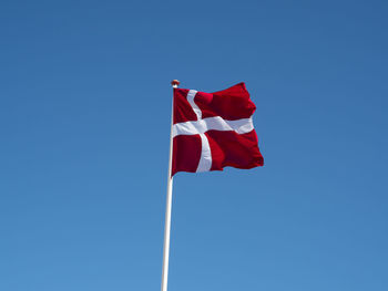 Low angle view of danish flag waving against clear blue sky